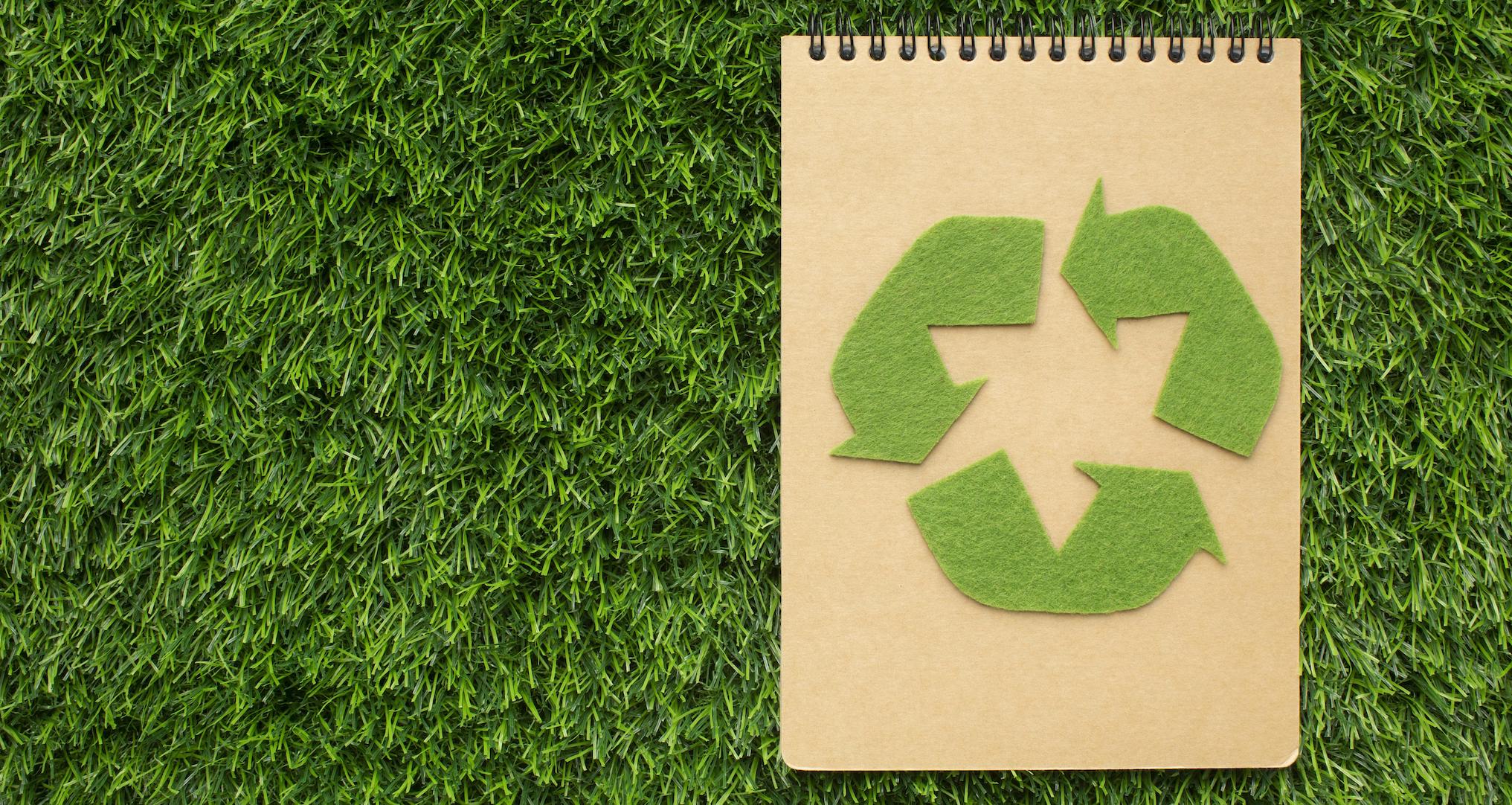 brown notebook with recycling logo on green grass background
